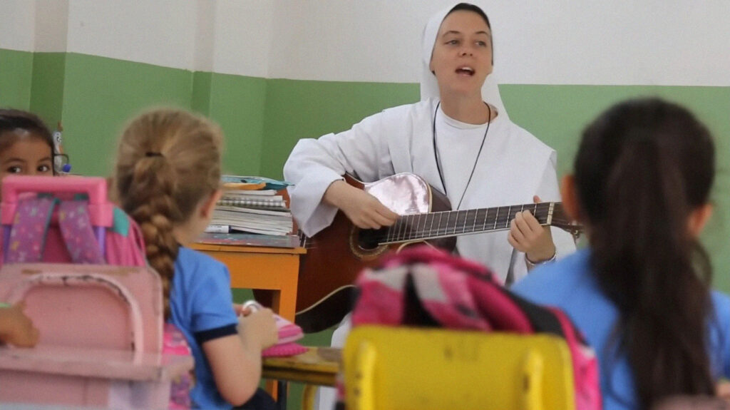 Ir. Clare toca violão para acalmar as crianças, após retornarem à sala de aula mais agitadas. agitadas para a sala de aula.